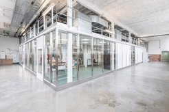 Ein geräumiges Labor mit verglasten Wänden in einer historischen Fabrikhalle sichtbaren Lüftungsrohren an der Decke in der linken oberen Bildecke.