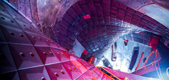 The interior of a futuristic, metallic structure featuring curved surfaces with geometric panels and bolts, illuminated by vibrant red and blue lighting, suggesting advanced technology.